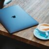 silver macbook beside white ceramic mug on brown wooden table