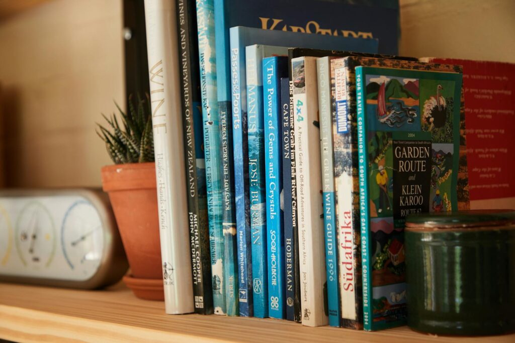 Wooden shelf filled with different interesting books near pots with green plants at home