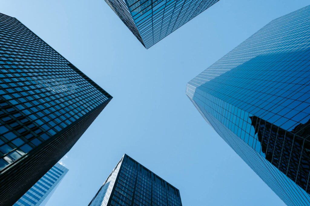 Low angle of high business towers with glass mirrored windows located in megalopolis downtown against blue sky