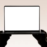 Hands hold up an open laptop with a blank screen.